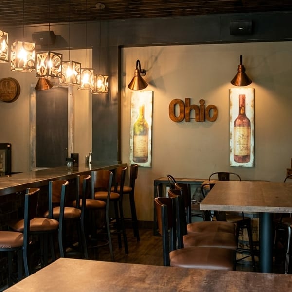 Cozy restaurant interior with a bar, wine rack, wooden tables, and "Ohio" wall decor.