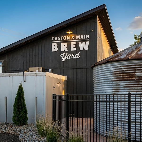 Exterior of Caston & Main Brew Yard, a dark building with a large rusty silo and blue sky.
