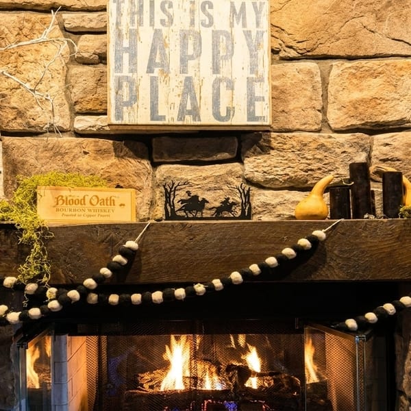 A stone fireplace with a wooden mantel decorated with gourds, moss, and a "This is My Happy Place" sign.